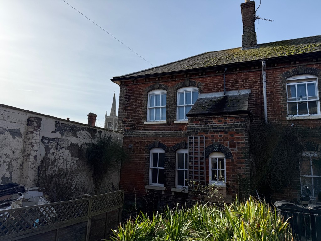 Lot: 127 - THREE-BEDROOM END-TERRACE COTTAGE FOR IMPROVEMENT - Alternative view of the front of the house with church in the background
